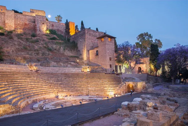 Illuminated Roman Theater with ancient stone seating beneath Málaga's Alcazaba at dusk
